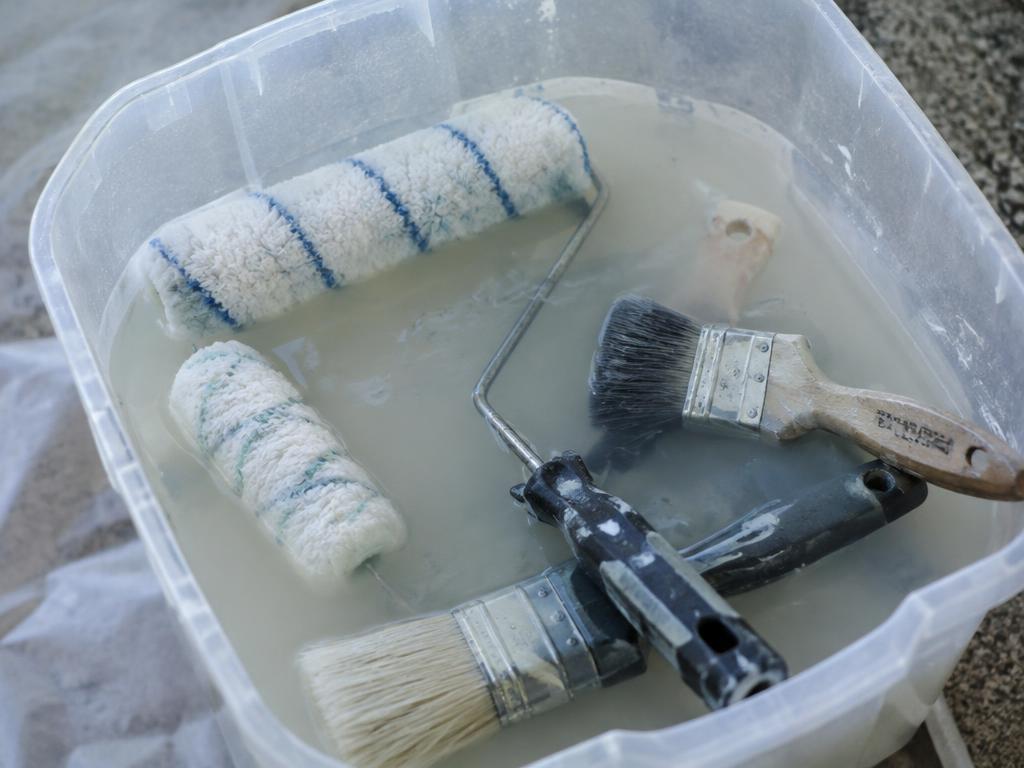 Paint rollers and brushes soaking in cloudy paint wash water