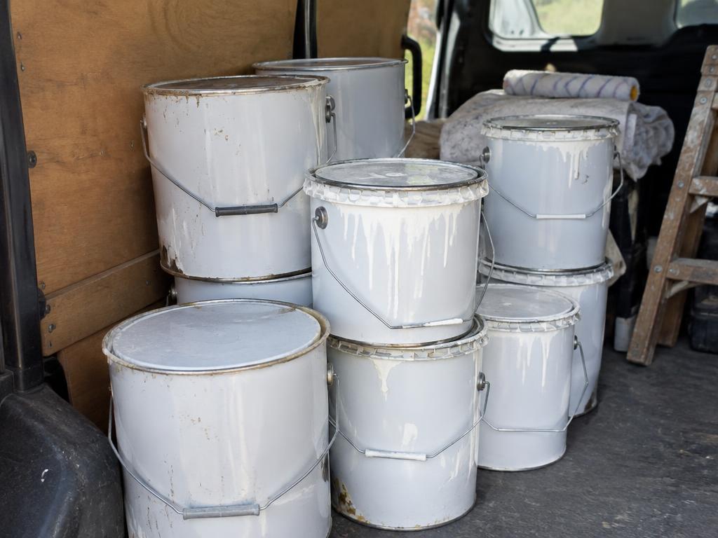Stacked used tins of white emulsion paint inside a decorator's van
